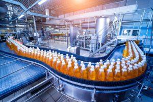Bottles of an orange liquid are conveyed through a clean industrial facility.